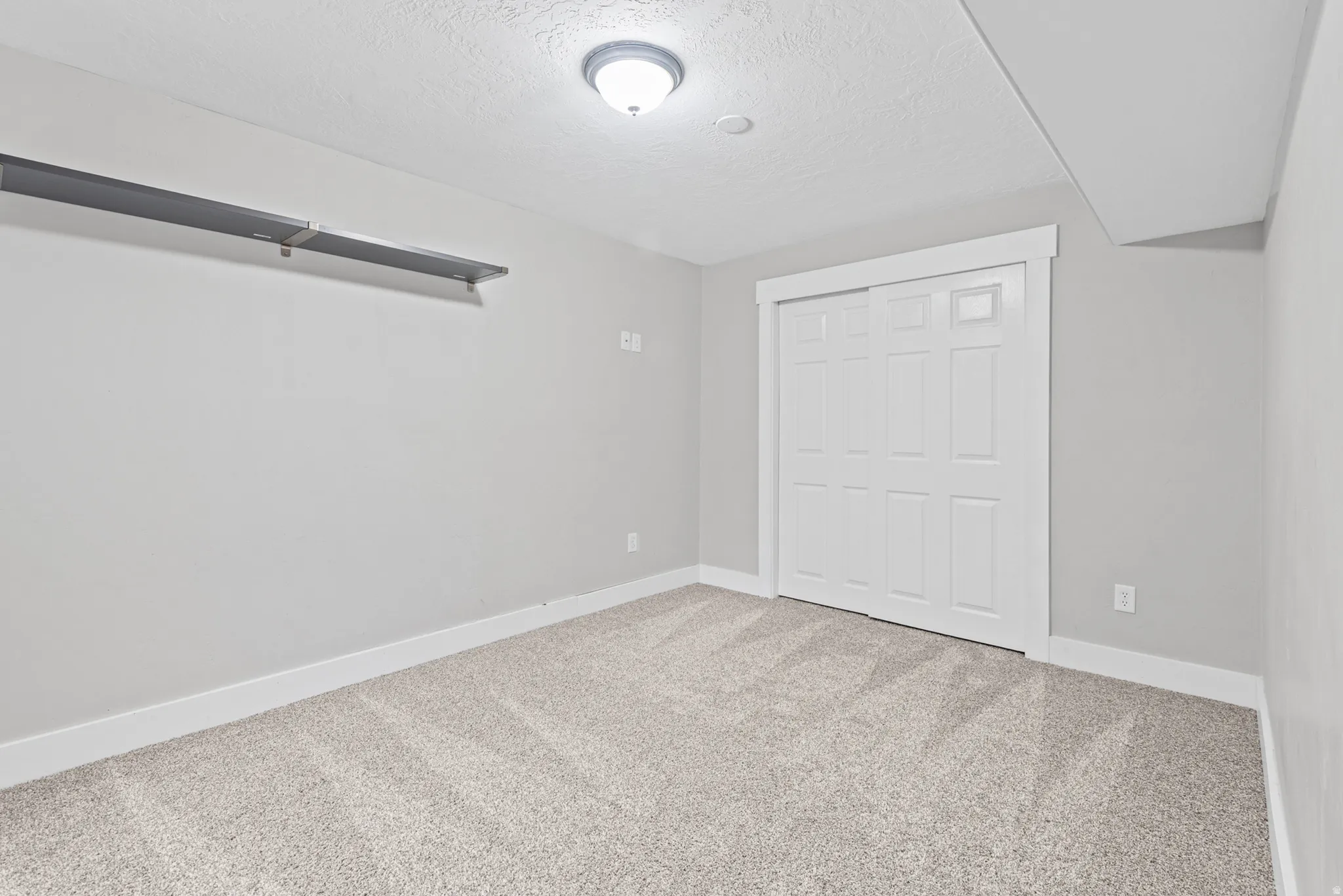 Neutral tone wall paint, textured carpet flooring, white trim, ceiling-mounted light fixture, and a sliding panel door