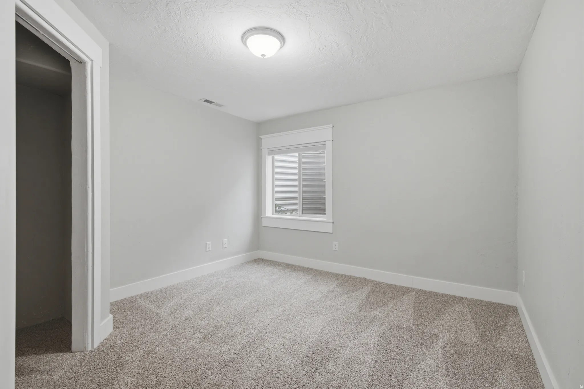 Bright secondary bedroom featuring neutral carpeting, white painted walls, and a shuttered window with natural light