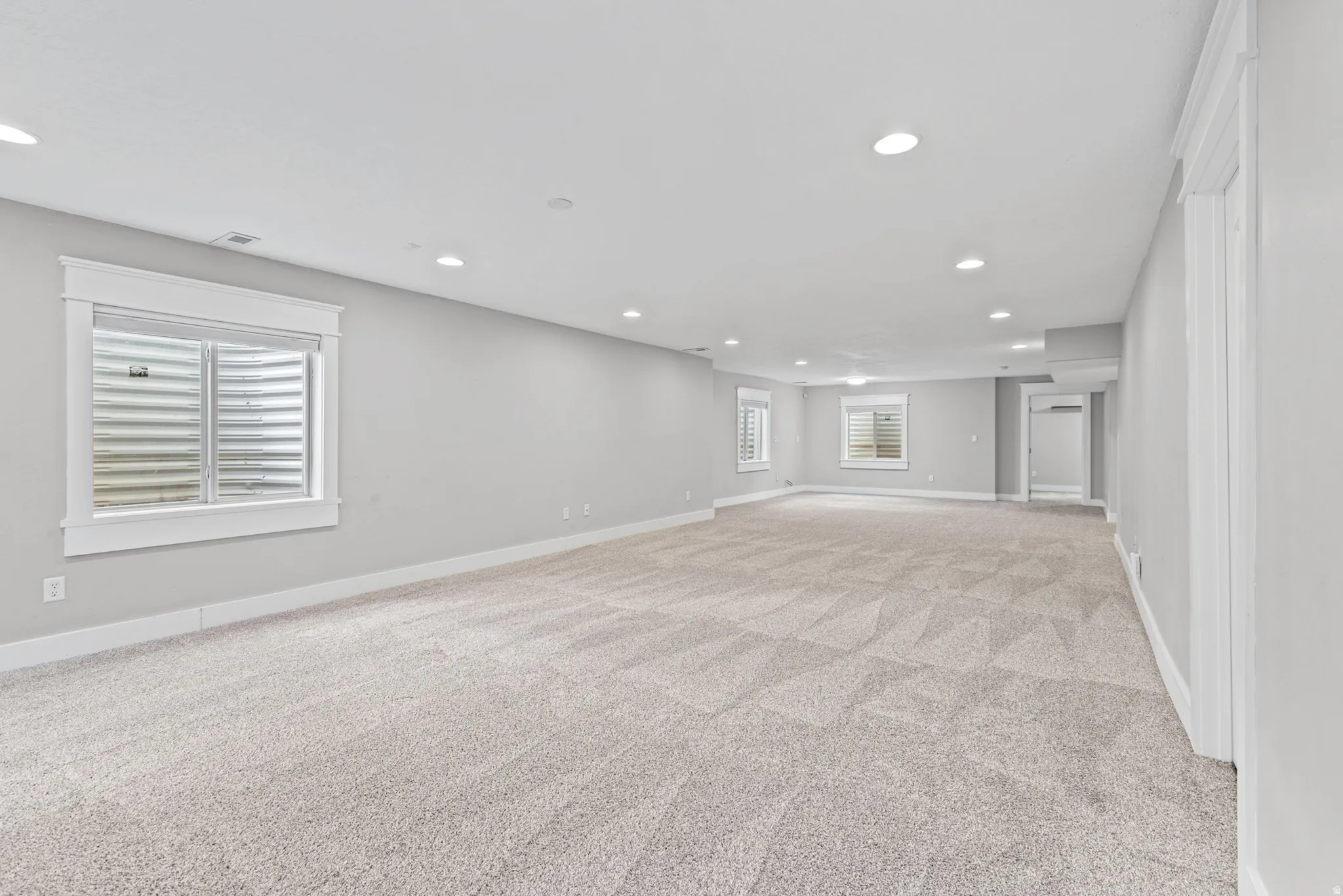 Spacious carpeted room with multiple recessed lights and three egress windows