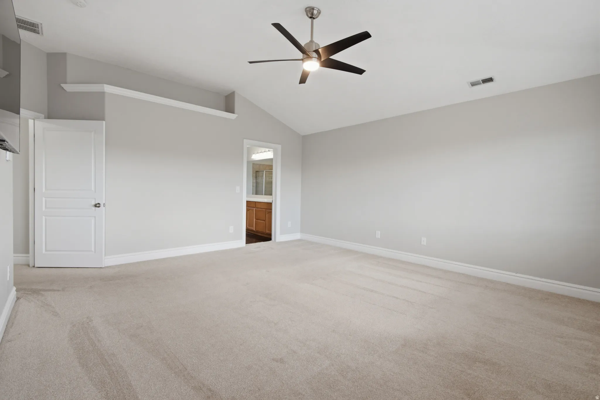 Vaulted ceiling, ceiling fan with integrated lighting, neutral carpet flooring, light gray wall tones, and an integrated wall shelf
