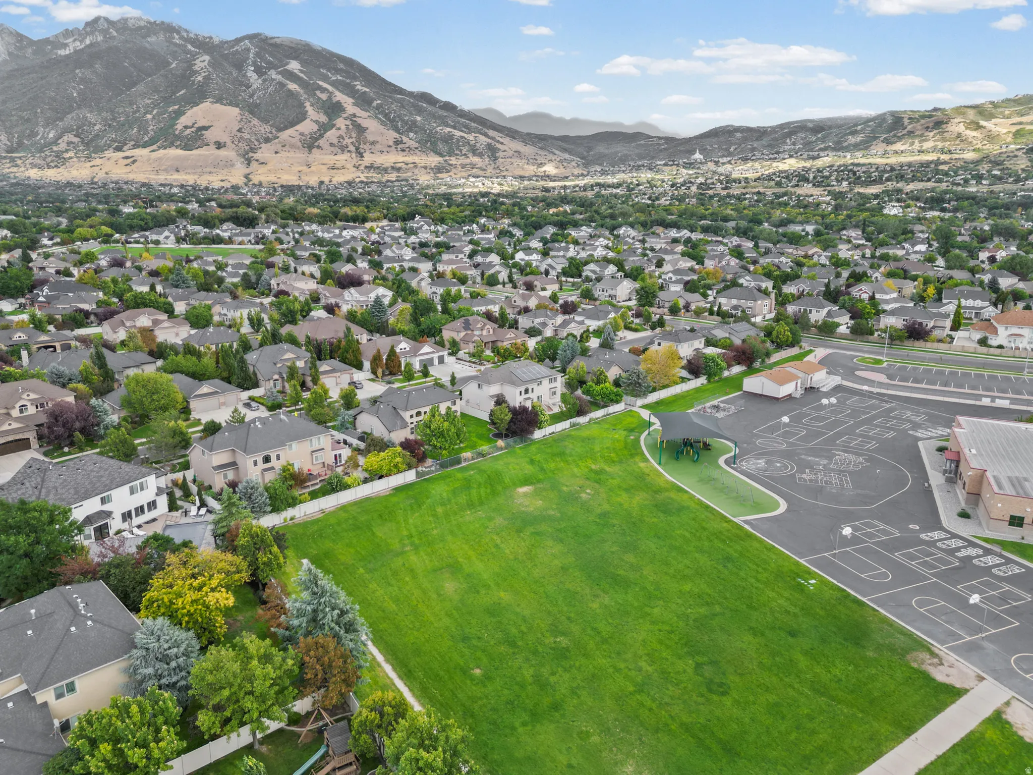 Expansive green space with manicured lawn, adjacent playground area, and surrounding residential structures
