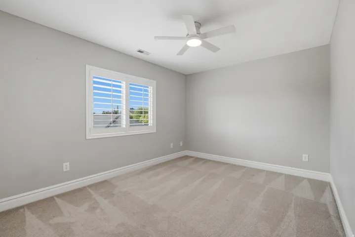 Neutral wall color, carpeted flooring, window with plantation shutters, and a ceiling fan with integrated lighting