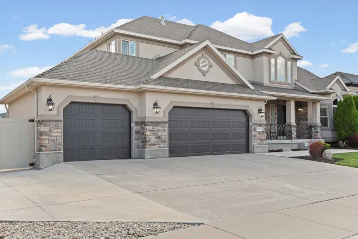 Stucco exterior with stone accents, a multi-car garage, concrete driveway, and front porch with wrought iron railings