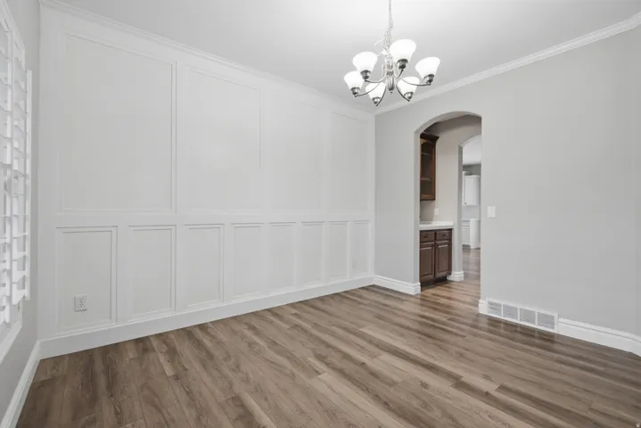 Wood-finish flooring, decorative wall paneling, crown molding, and a chandelier illuminate this versatile space