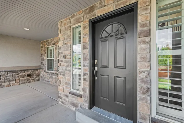 Stone veneer exterior with stucco accents, paneled entry door with transom window, and plantation shutters