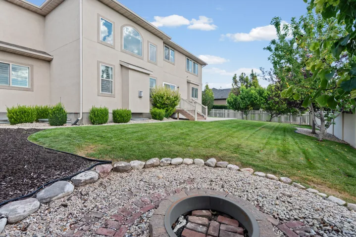 Expansive backyard with a manicured lawn, established trees, and a built-in fire pit with stone and brick accents