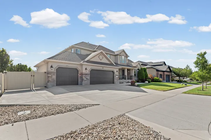 Two-story stucco and stone exterior featuring a multi-car garage, extensive concrete driveway, and a fenced side yard with gate access