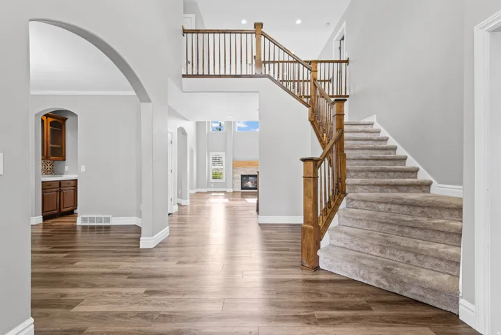 Two-story entryway with wood-finish flooring, a carpeted staircase with wood railing, and an arched doorway leading to built-in cabinetry
