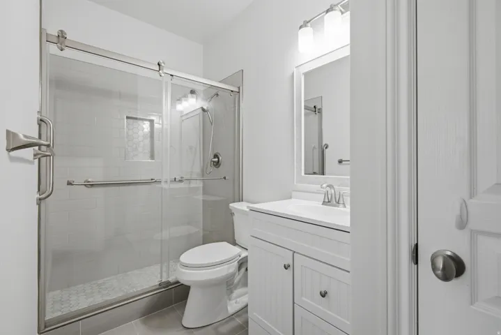 Fully tiled shower with sliding glass door, built-in shelving, and hexagonal floor tiles