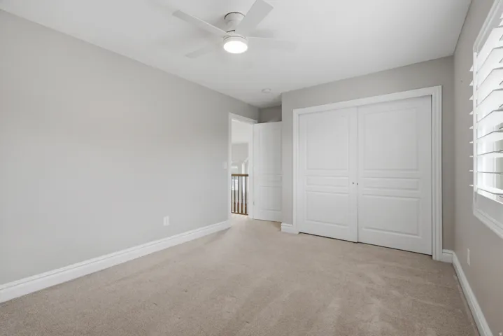 Plush carpeting, neutral wall tones, white bi-fold closet doors, ceiling fan with integrated lighting, and window with plantation shutters