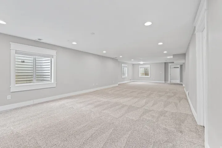 Spacious carpeted room with multiple recessed lights and three egress windows