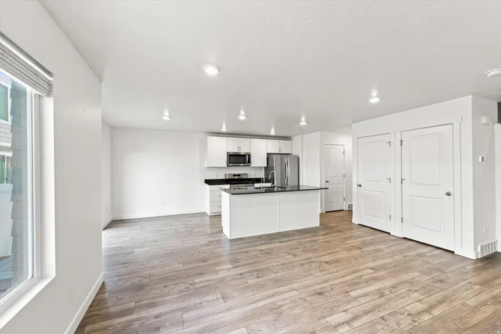 Open-concept living space featuring wood-finish flooring, recessed lighting, and a kitchen with white cabinetry, a central island, and stainless steel appliances