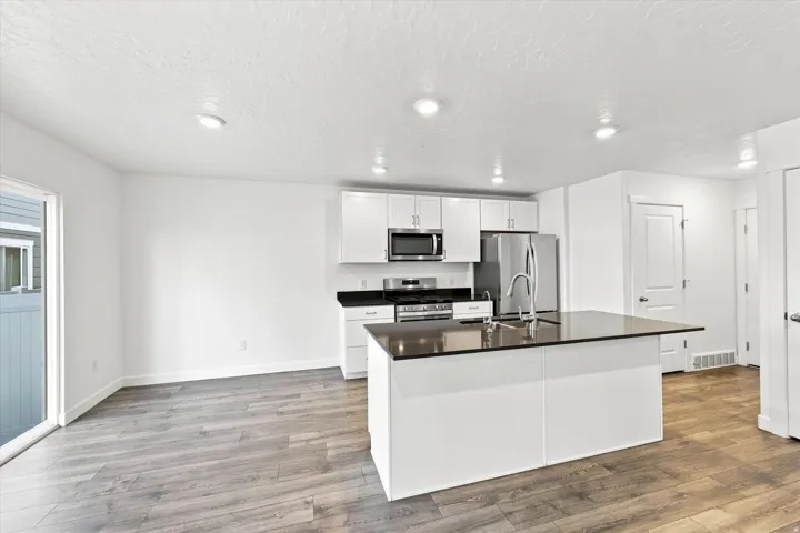 Modern kitchen featuring white cabinetry, stainless steel appliances, a center island with a dark countertop, and recessed lighting