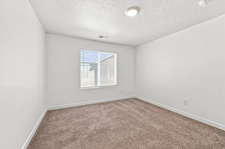Neutral paint tones, textured ceiling, flush mount ceiling light, window with blinds, and carpet flooring
