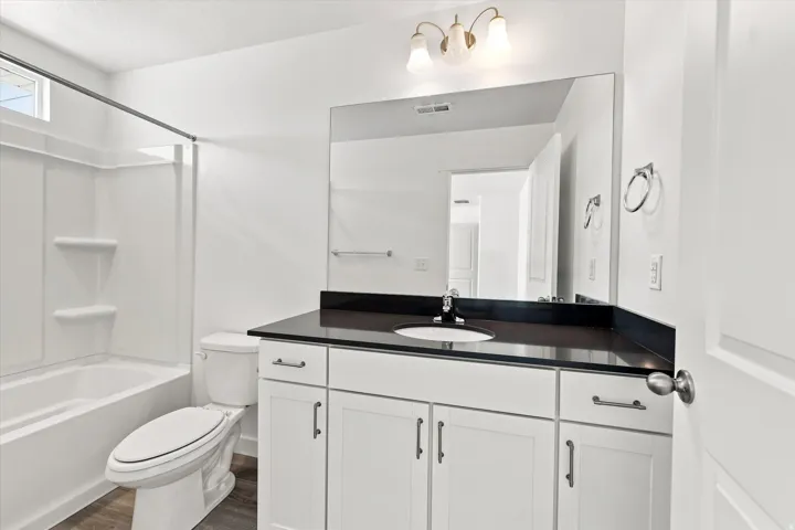 White vanity with dark countertop, undermount sink, and wall-mounted mirror