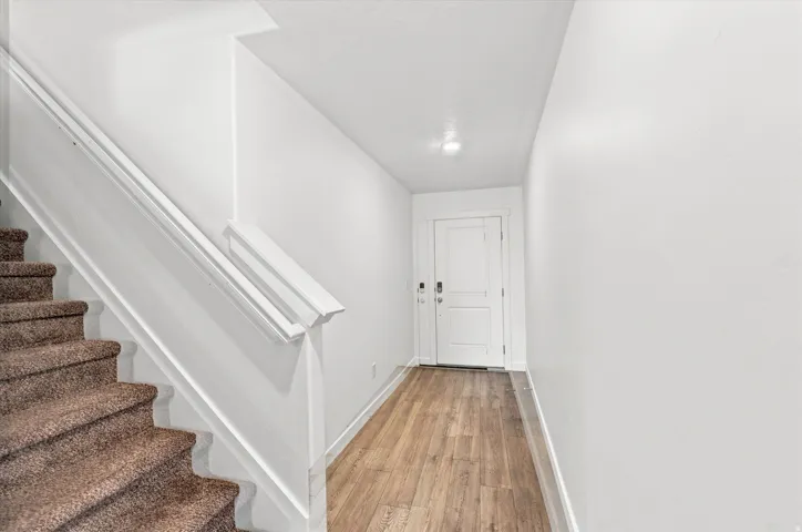 Entryway featuring wood-finish flooring, a two-panel door with smart lock, flush mount lighting, and a carpeted staircase with white handrail