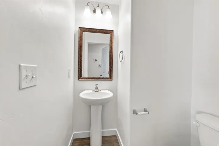 Pedestal sink with chrome faucet, framed mirror, and wall-mounted vanity lighting