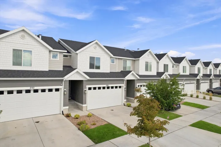 Modern townhome exterior featuring light gray siding, white shake siding, dark gray roofing, white garage doors, and individual entryways