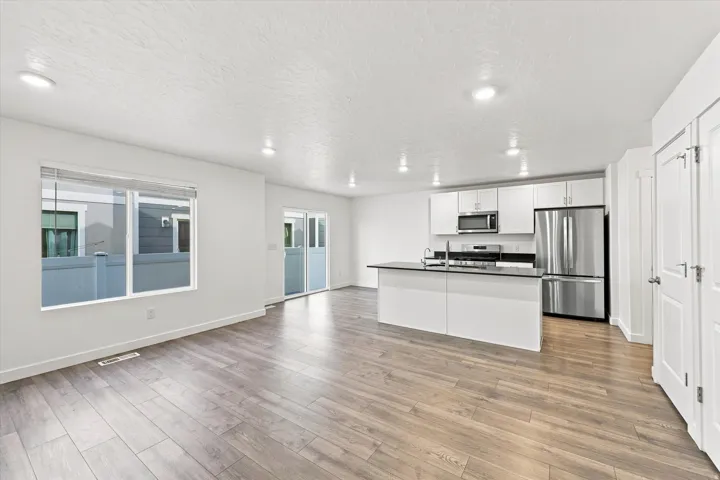 Open concept living space featuring wood-finish flooring, white walls, recessed lighting, and a kitchen island with dark countertops