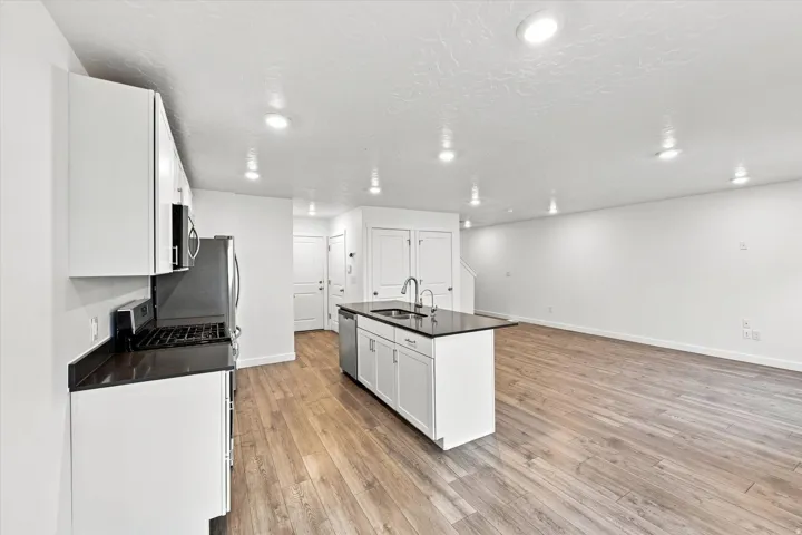 Kitchen island with integrated sink, white cabinetry, dark countertops, stainless steel appliances, and wood-finish flooring