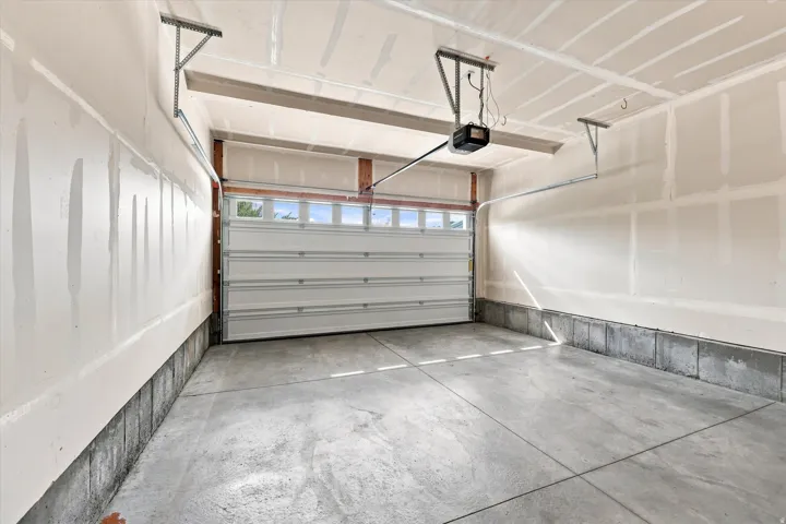 Concrete flooring, white overhead garage door, built-in window panels, automatic garage door opener, and bracketed ceiling supports