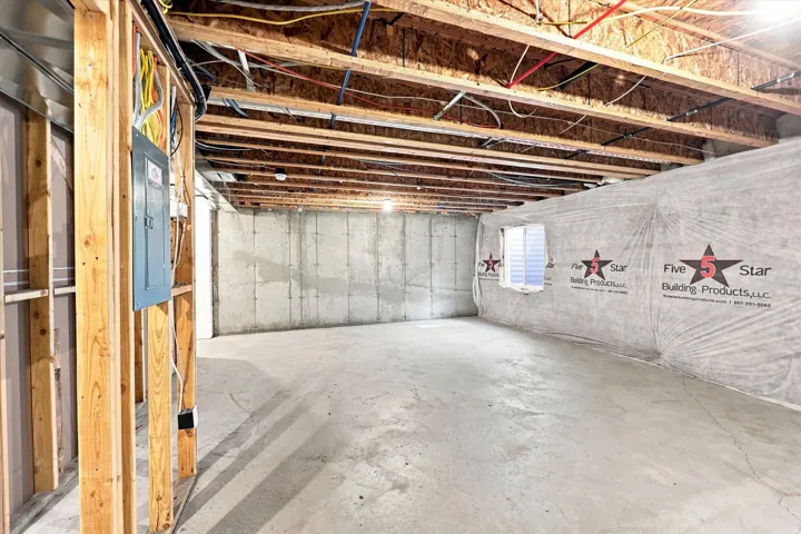 Unfinished basement featuring exposed wood joists, concrete foundation walls, a poured concrete floor, and an electrical service panel