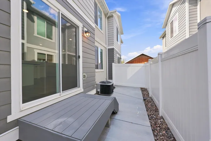 Sliding glass door access, exterior wall lantern, concrete patio, privacy fencing, and gravel landscaping