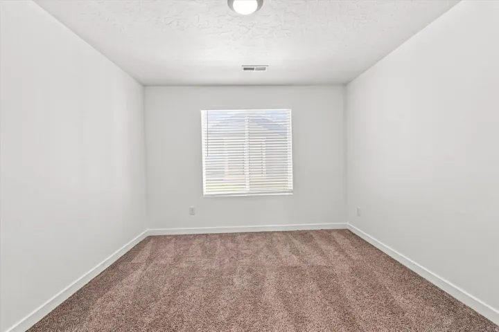 Neutral-toned wall-to-wall carpeting, white painted walls, and a window with horizontal blinds