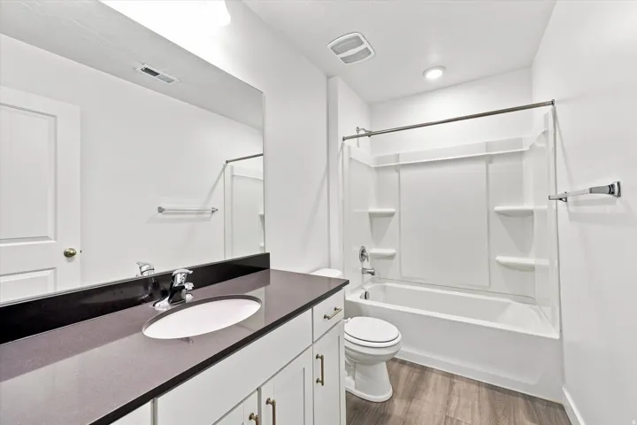Vanity with integrated sink, dark countertop, white shaker-style cabinetry, and wood-finish flooring