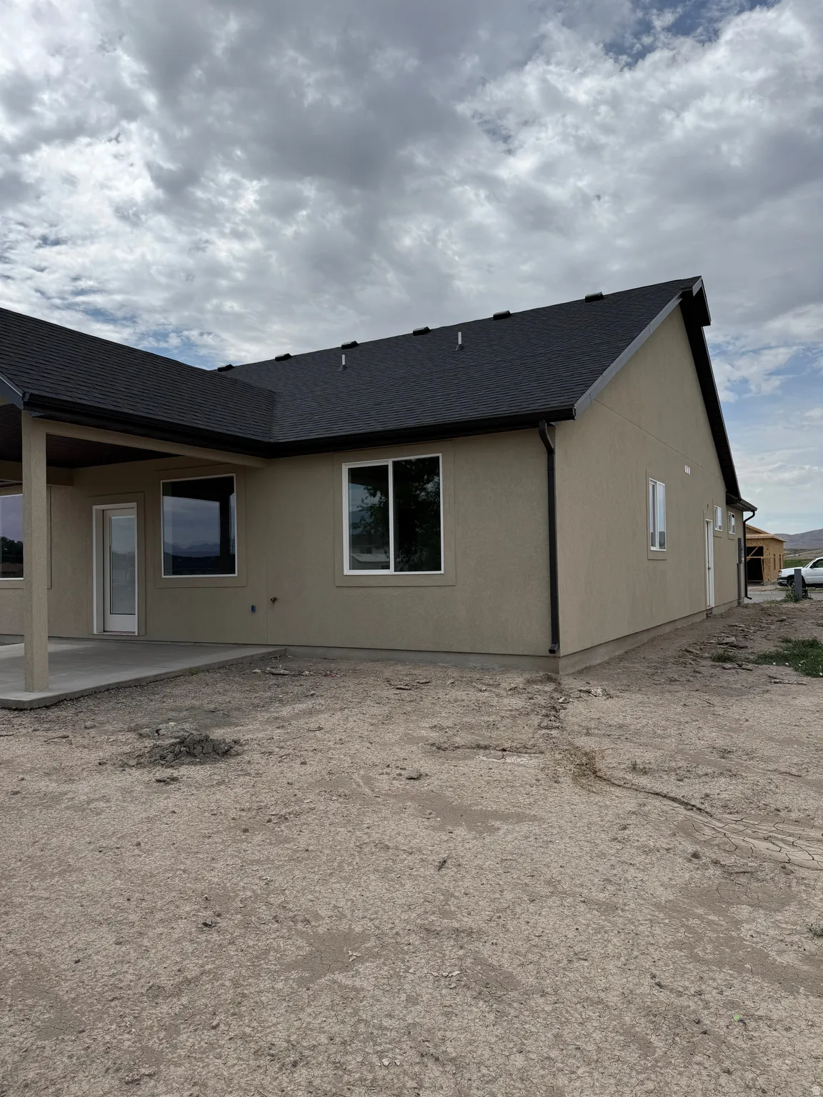 Stucco exterior with a covered patio, multiple windows, and a dark shingle roof