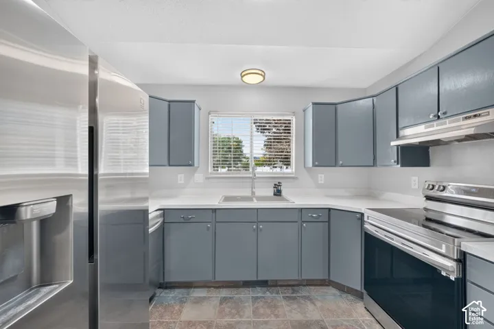 Kitchen featuring gray cabinetry, light-toned countertops, stainless steel appliances, and a window above the sink