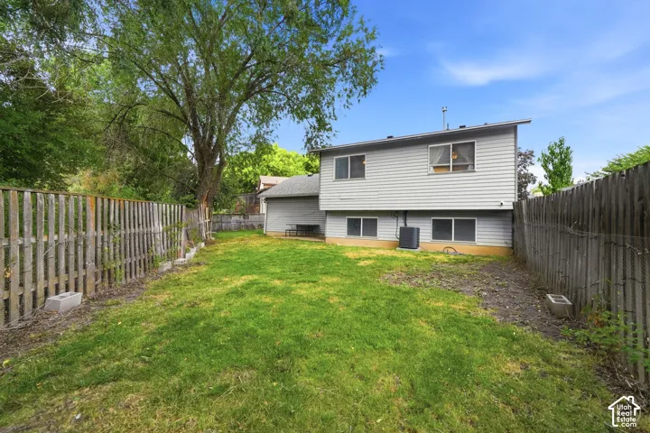 Expansive backyard featuring a manicured lawn, established perimeter fencing, mature trees, and a vinyl-sided exterior with multiple windows