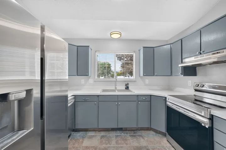 Kitchen featuring gray cabinetry, light-toned countertops, stainless steel appliances, and a window above the sink