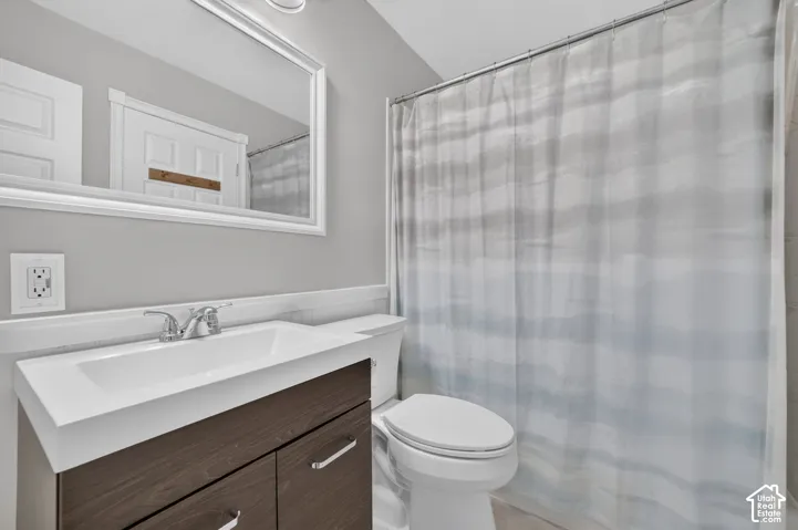 Bathroom featuring a wood-finish vanity, integrated sink, chrome faucet, wall-mounted mirror, and a toilet
