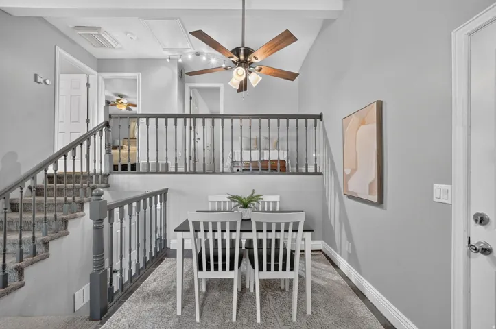 Vaulted ceiling with a ceiling fan, carpeted staircase with painted wood railings, and an open loft area