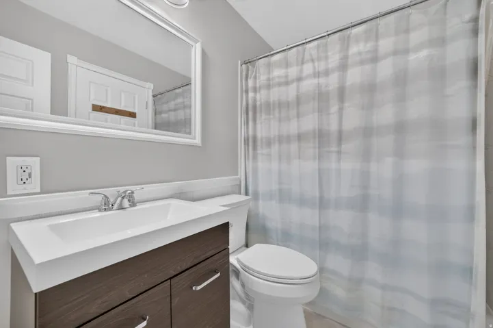 Bathroom featuring a wood-finish vanity, integrated sink, chrome faucet, wall-mounted mirror, and a toilet