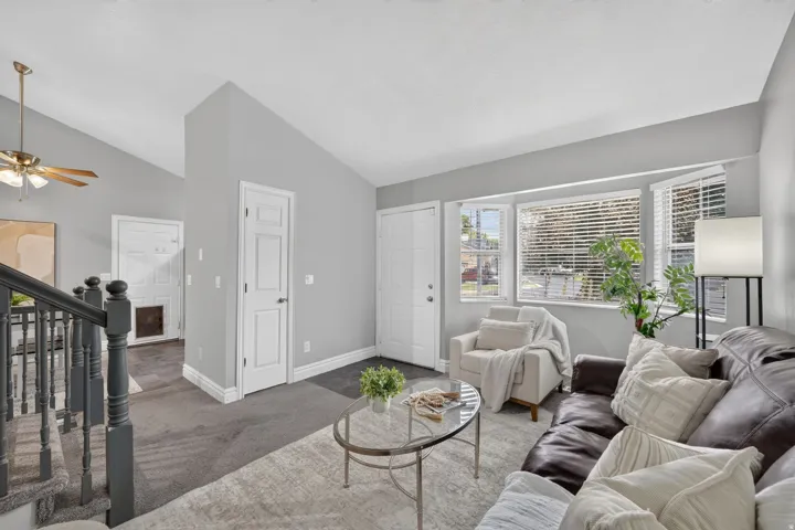 Vaulted ceiling with a ceiling fan, bay window with blinds, carpet flooring, and a staircase with painted wood railings