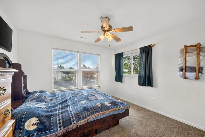 Spacious bedroom featuring large double-hung windows with blinds, ceiling fan with integrated lighting, wood-finish flooring, and neutral wall finishes