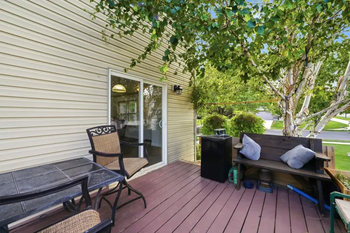 Expansive wood-finish deck with sliding glass door access, exterior wall-mounted lighting, and mature trees overhead