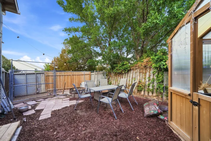 Enclosed backyard area featuring a wood fence, chain-link fence, woodchip ground cover, and a wood-framed structure with translucent panels