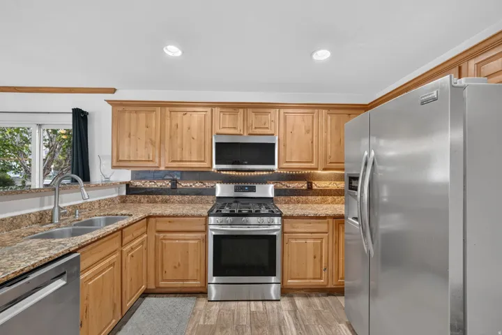 Wood-finish cabinetry, stainless steel appliances, dual basin sink, and granite-style countertops