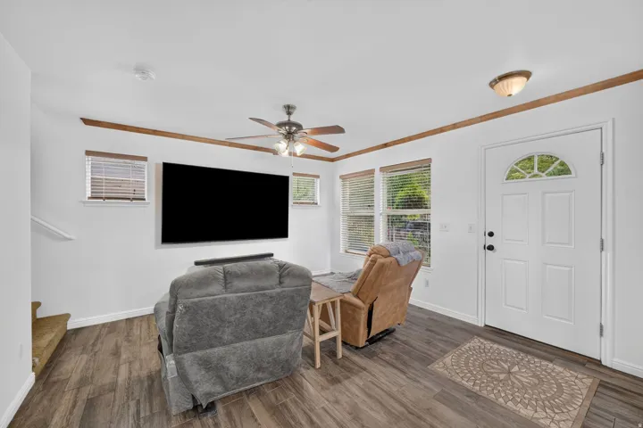 Wood-finish flooring, white paneled entry door with arched window, decorative crown molding, and ceiling fan with integrated lighting