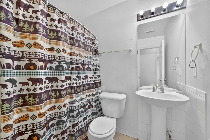 White pedestal sink with chrome faucet, wall-mounted mirror, and vanity lighting