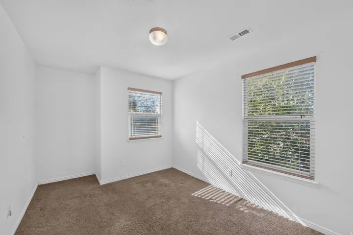 Neutral wall paint, carpet flooring, two windows with blinds, and a flush-mount ceiling light
