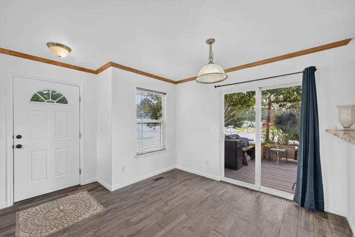 Wood-finish flooring, white paneled entry door with an arched glass insert, single window with blinds, sliding glass patio door, and a built-in light fixture