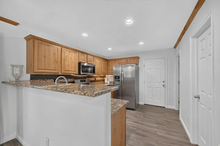 Kitchen with wood-finish cabinetry, stone countertops, stainless steel appliances, and recessed lighting