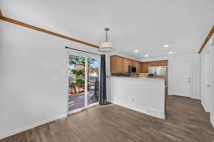Wood-finish flooring throughout, sliding glass door to exterior deck, wood cabinetry with stainless steel appliances, recessed ceiling lights, and overhead pendant light fixture