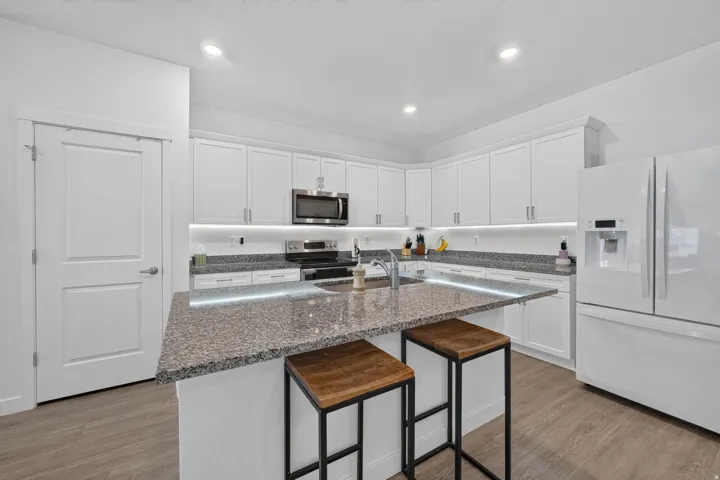 Modern kitchen featuring white cabinetry, stainless steel appliances, recessed lighting, wood-finish flooring, and a central island with a sink and stone countertop
