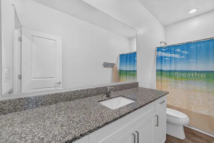 Modern bathroom featuring a gray speckled stone countertop, white cabinetry with hardware accents, rectangular undermount sink, and chrome faucet