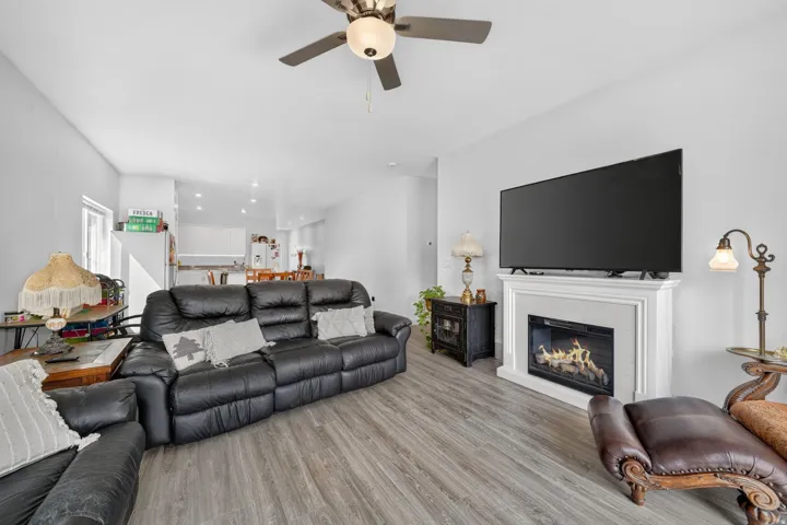 Bright living area featuring wood-finish flooring, a white mantel fireplace, and a ceiling fan with integrated lighting